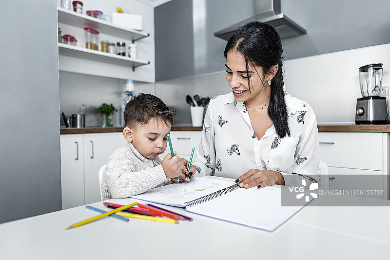 微笑的年轻西班牙裔女性和儿子在画册上用铅笔绘画图片素材