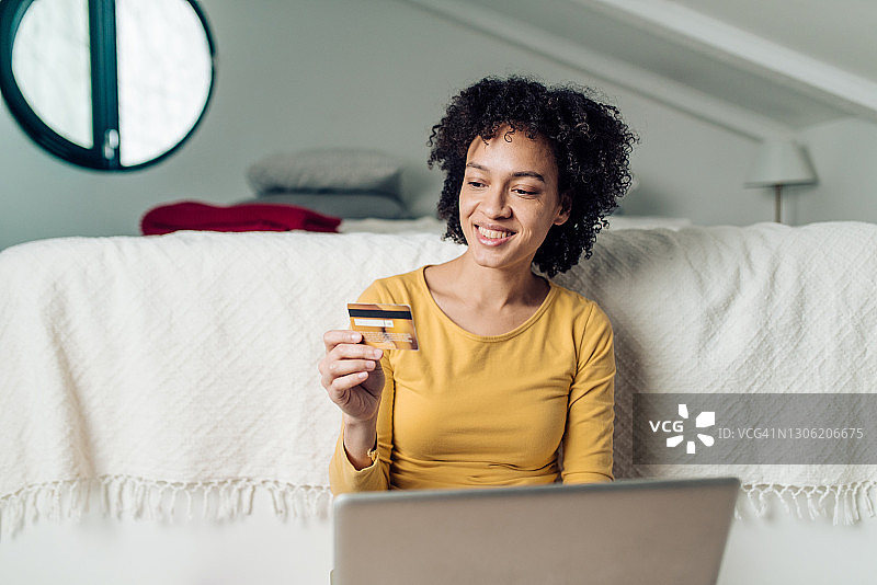 快乐的非裔美国年轻女人在卧室里网购图片素材