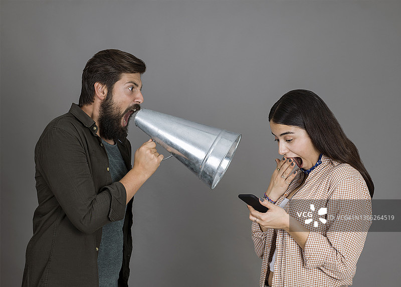 愤怒的年轻人拿着扩音器对着用手机不理睬他的女友尖叫图片素材