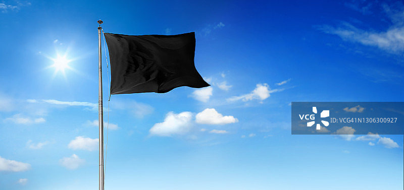 在晴朗的天空下挥舞的旗杆上的黑色空白旗帜图片素材