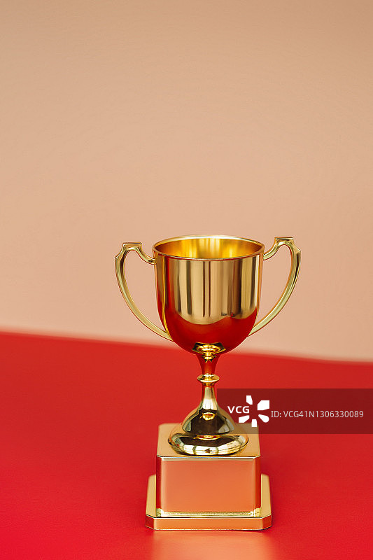 红色桌子上米色墙壁旁的金色高脚杯正面照：目标达成概念图片素材