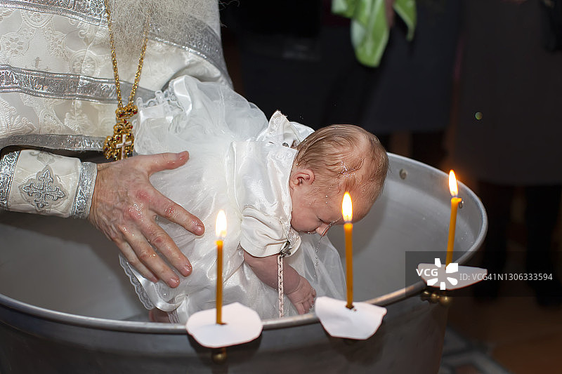 东正教儿童洗礼仪式：牧师的手在洗礼盆中为婴儿洗礼图片素材