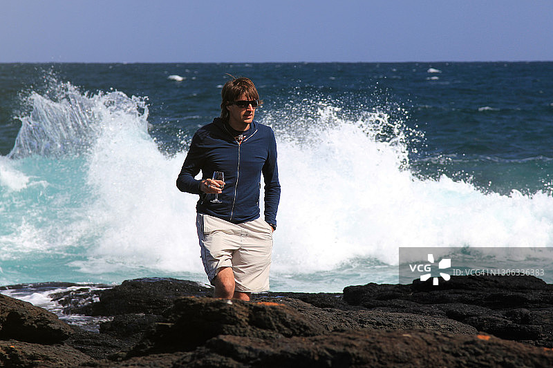 在海边手持一杯白葡萄酒行走的中年男人图片素材