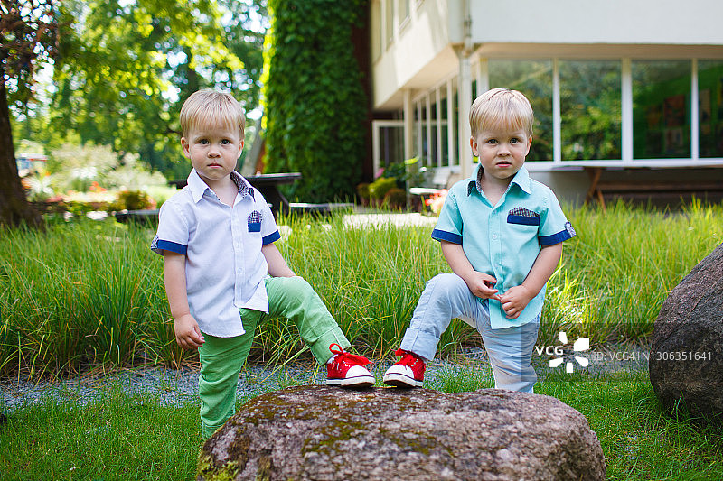 可爱的幼儿双胞胎兄弟在花园里散步，在石头上摆姿势图片素材