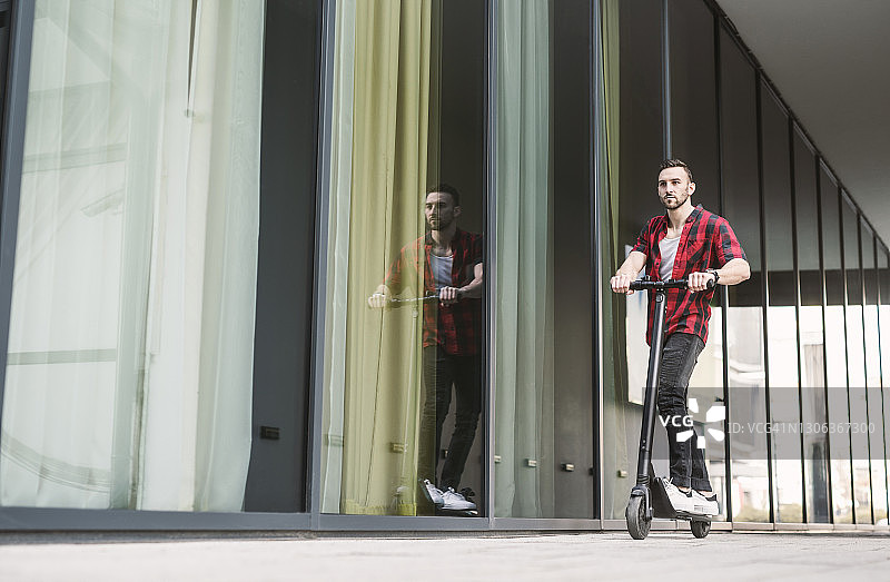 有魅力的男人在城市背景下骑电动滑板车图片素材