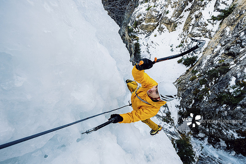 俯视：男性攀冰者挥舞冰镐攀登壮观的冰冻瀑布图片素材