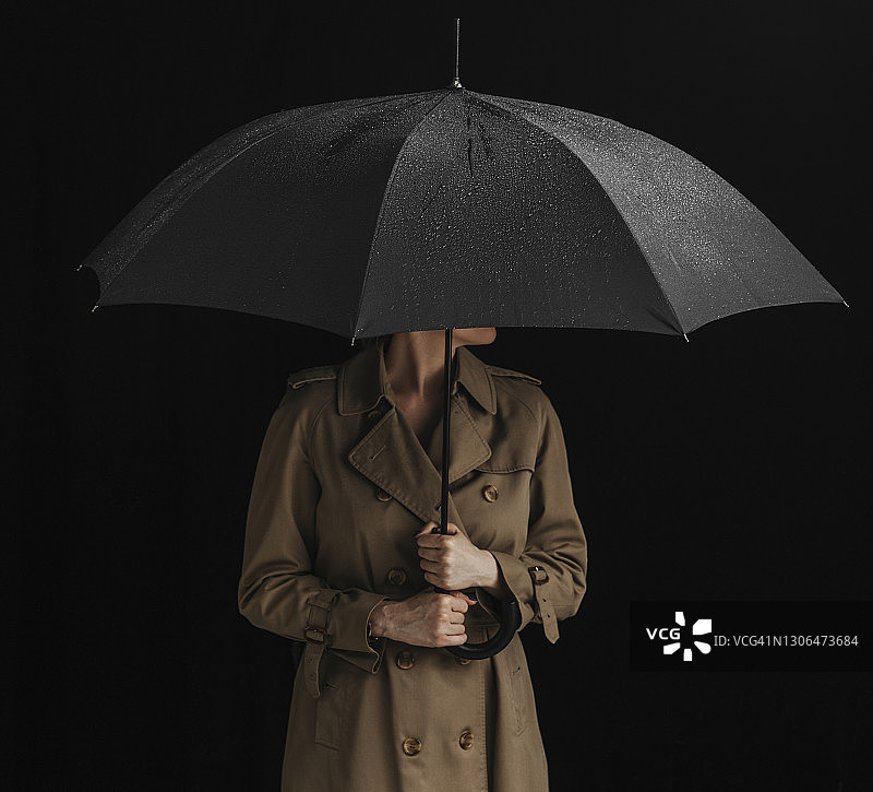 匿名女子穿着雨衣，拿着一把打开的黑雨伞（工作室拍摄）图片素材