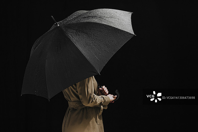 匿名女子穿着雨衣，拿着一把打开的黑雨伞（工作室拍摄）图片素材