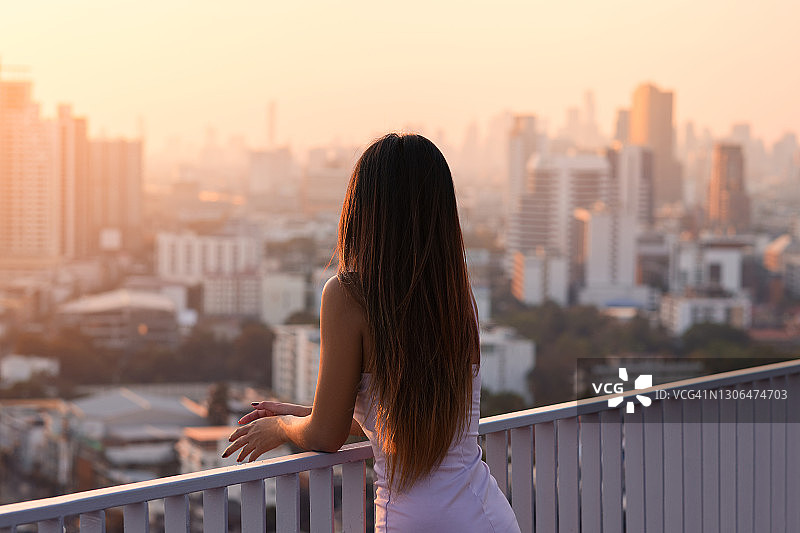 美丽的亚洲女人在日落时分从屋顶看着城市图片素材