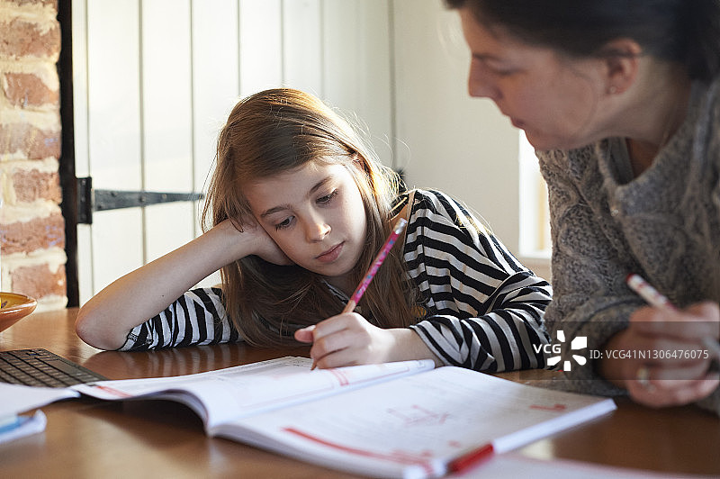 母亲在厨房的桌子上帮助小女儿做作业图片素材