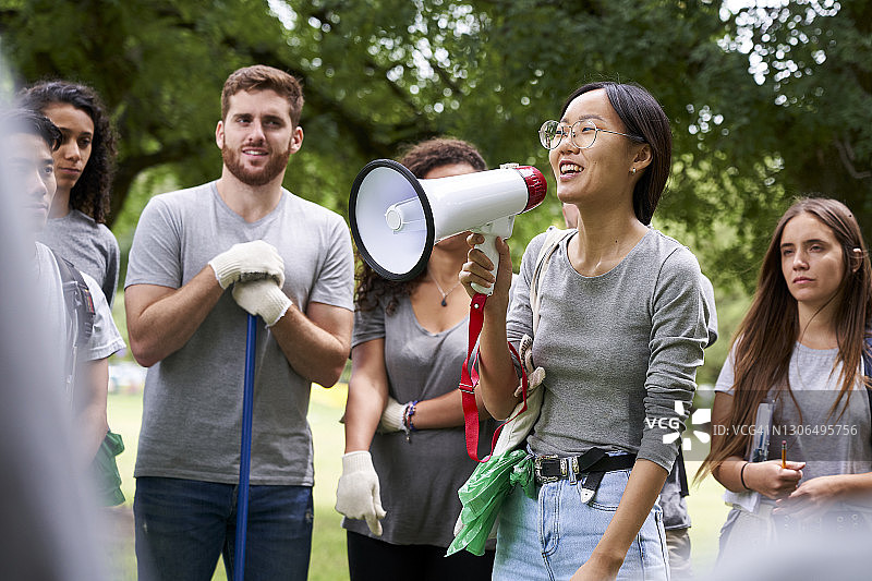 年轻女志愿者在公园里和朋友们站在一起，用扩音器讲话图片素材