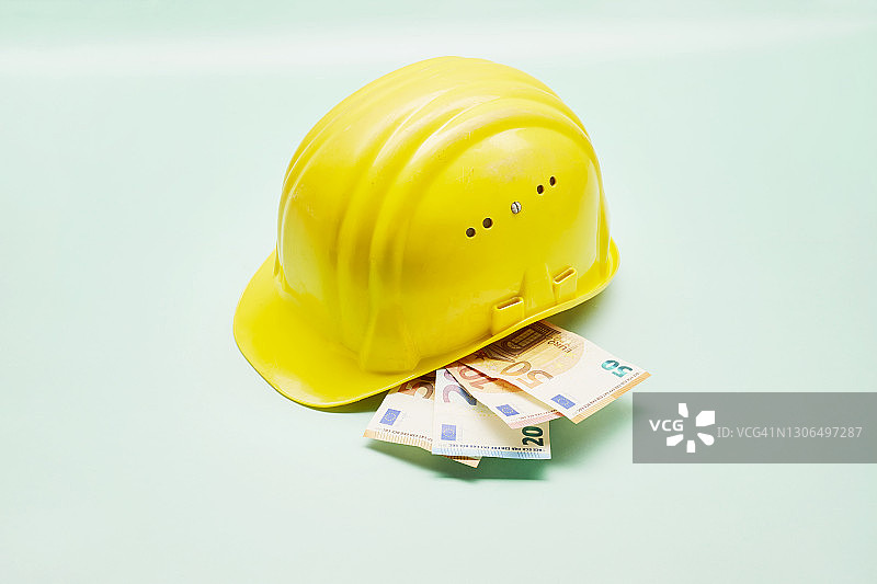 黄色建筑头盔和欧元纸币的绿色背景静物图片素材
