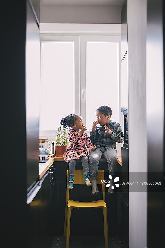 微笑的男孩和女孩在家中厨房台面上吃水果图片素材