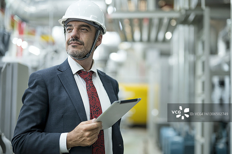 自信的商人站在工厂里，手持平板电脑，在食品加工厂的锅炉房控制室工作图片素材