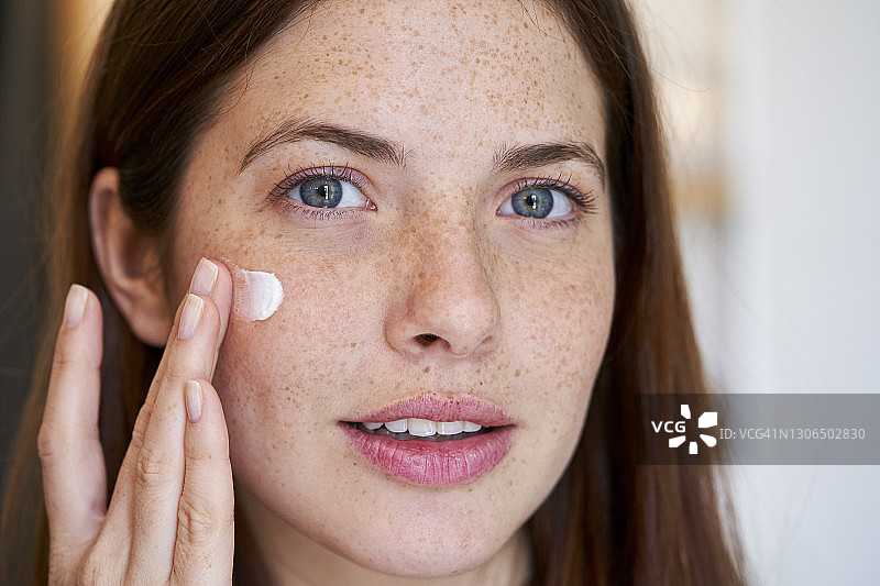 微笑的年轻女子在脸上涂抹护肤霜图片素材