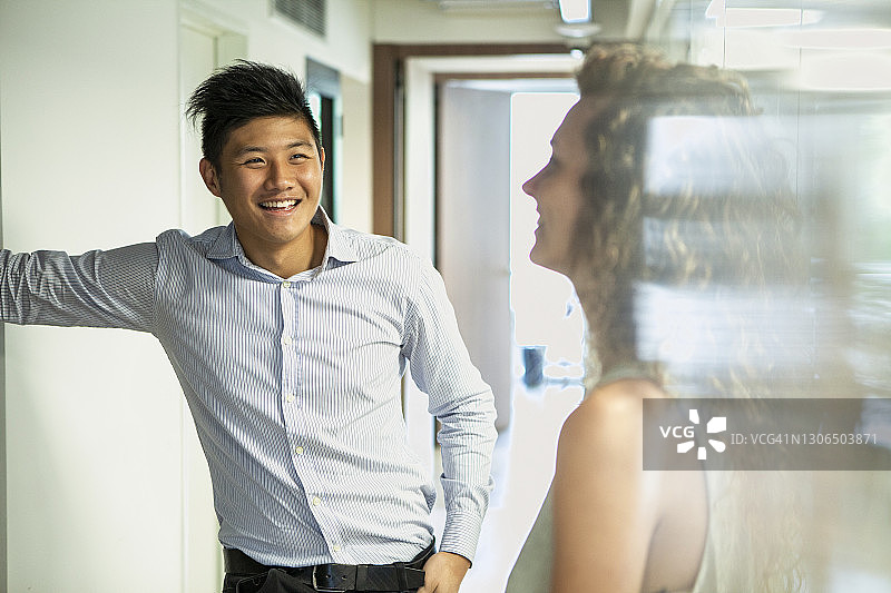 微笑的商人与女同事在办公室走廊交谈图片素材