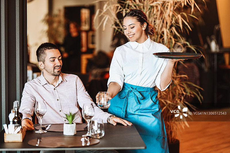 微笑的女服务员给餐厅男顾客端饮料图片素材