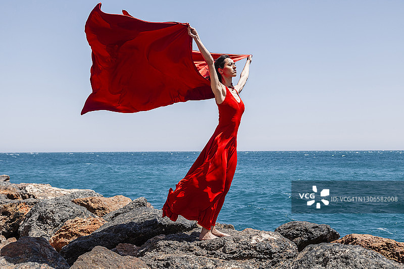 阳光明媚的日子里，优雅的舞者在海滩岩石上舞动丝巾图片素材
