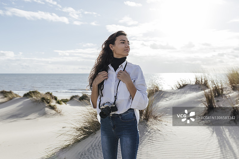 沙丘上拿着复古相机看天空的年轻女人图片素材