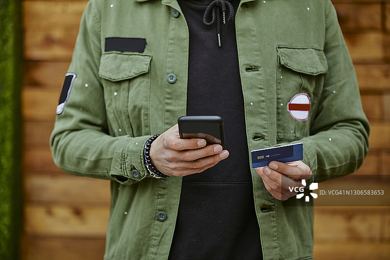 穿着夹克的男人拿着智能手机，通过信用卡进行在线支付图片素材