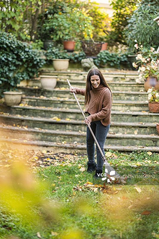 在后院花园里用耙子清扫的穿着暖和衣服的女人图片素材