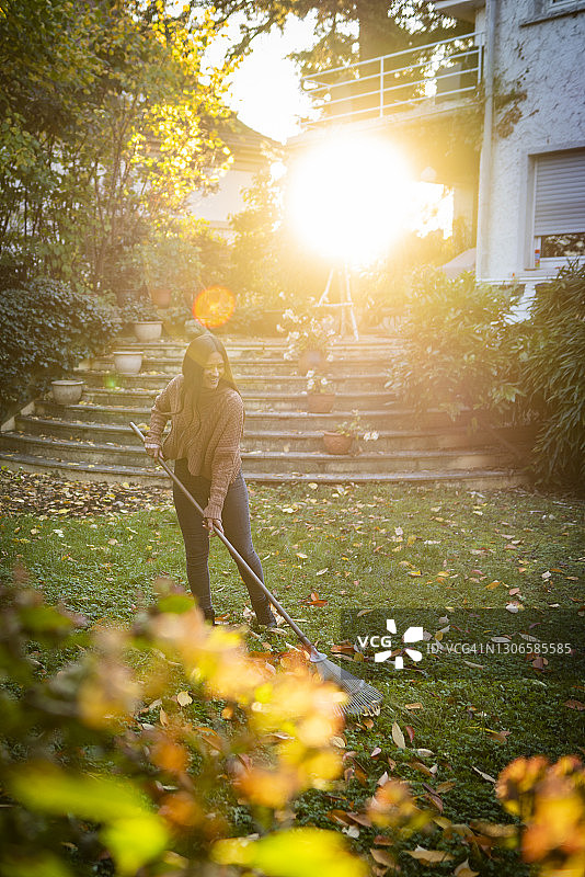 在阳光明媚的花园里用扫帚扫地的女人图片素材