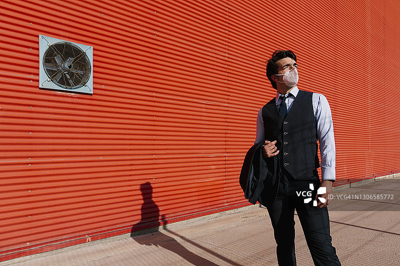 疫情期间，商人穿着西装站立在橙色墙前图片素材