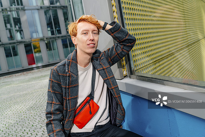 红发男人站在人行道上，手放在头发上，背景是建筑物图片素材