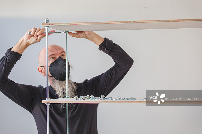 新冠肺炎隔离期间在家工作：男人组装胶合板工业风置物架图片素材