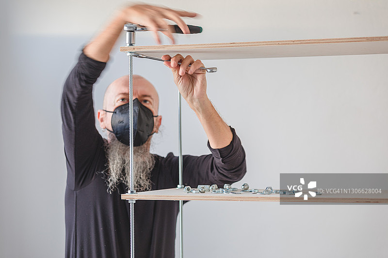 新冠肺炎隔离期间在家工作：男人组装胶合板工业风置物架图片素材