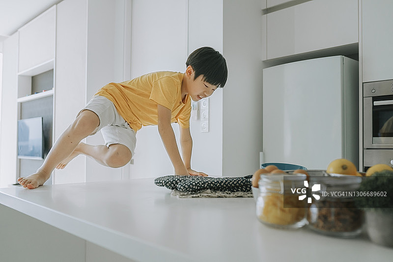中国籍调皮男孩爬上家里的厨房柜台玩耍图片素材
