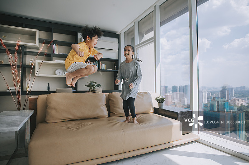 快乐的中国小男孩和小女孩在沙发上跳跃图片素材