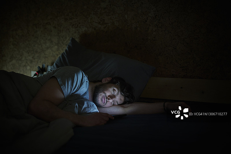 在床上玩智能手机的男人图片素材