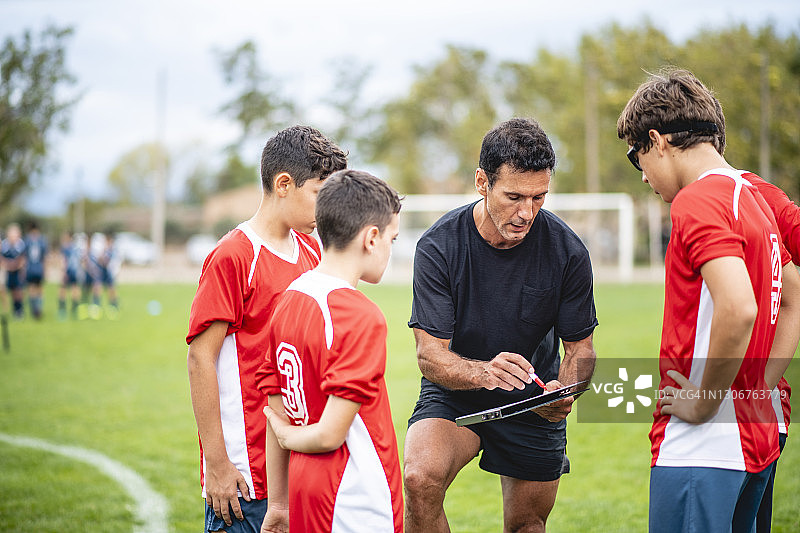 微笑的教练向红队足球运动员展示比赛图图片素材