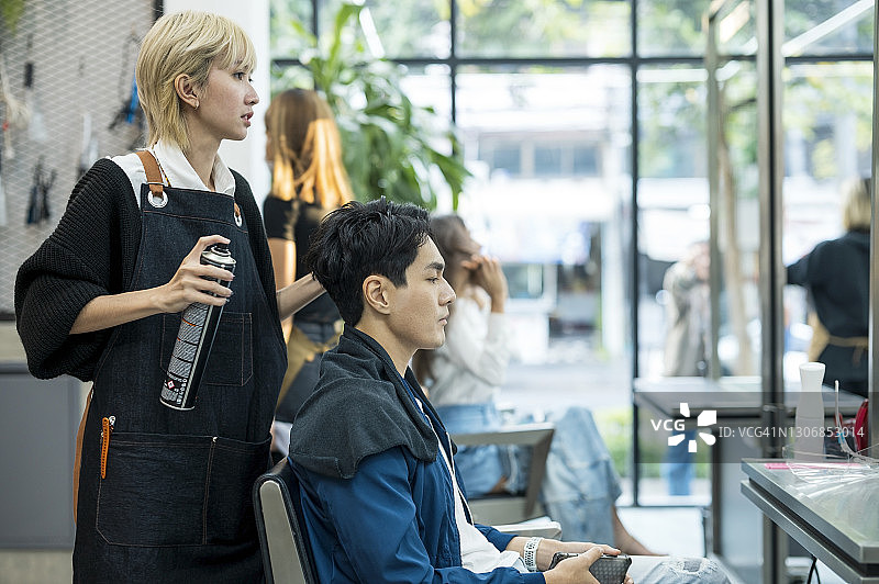 亚洲女性美发师在美发沙龙用发胶为顾客做头发图片素材