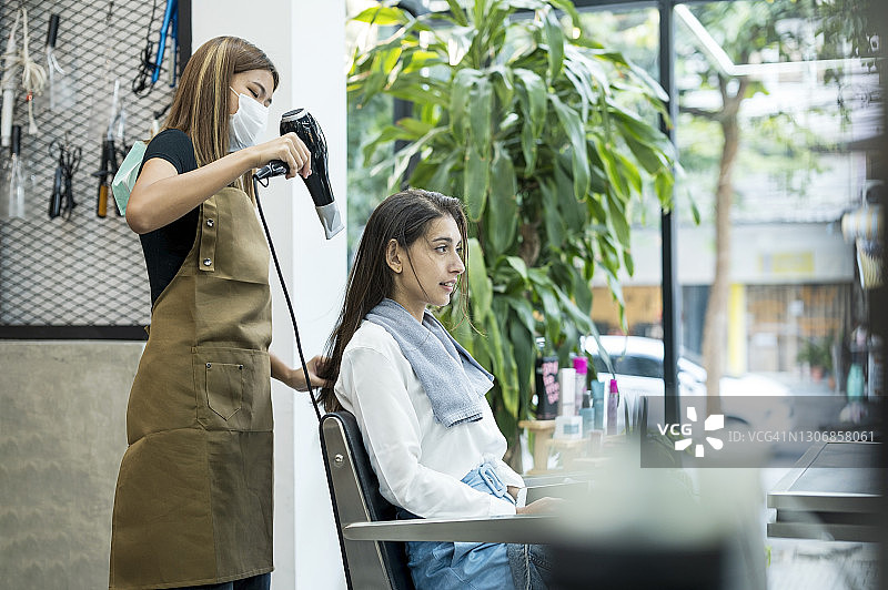 在美容美发沙龙，理发师在头发护理后为顾客吹干头发。美容美发沙龙业务。图片素材