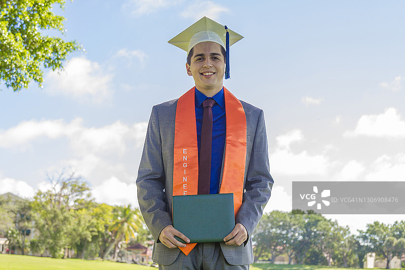 在美国毕业典礼上，戴着帽子和礼袍的快乐英俊拉丁裔男学生肖像图片素材