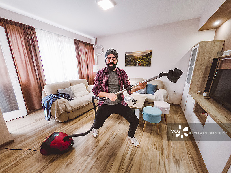 年轻男人用吸尘器清洁房间，快乐地跳舞图片素材