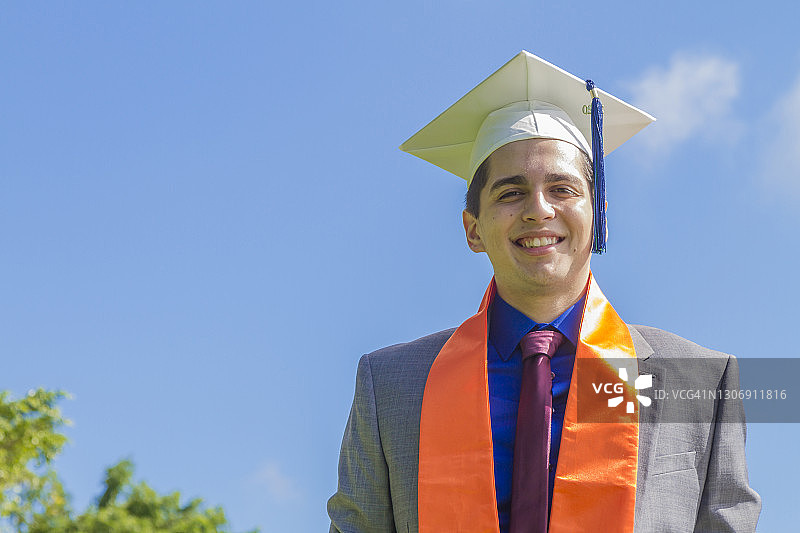 在美国毕业典礼上，戴着帽子和礼袍的快乐英俊拉丁裔男学生肖像图片素材