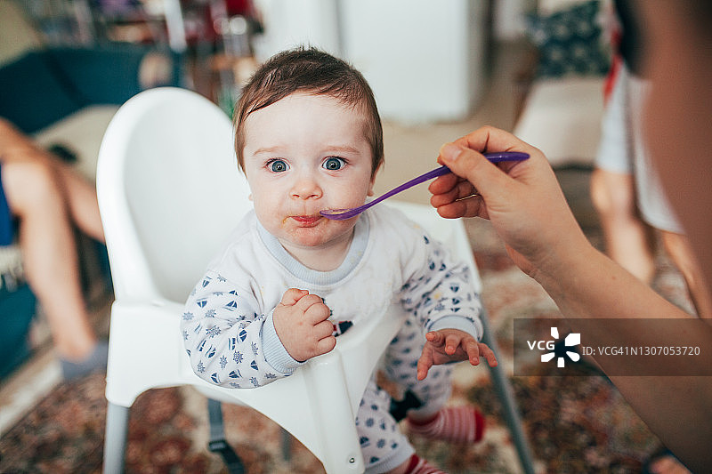 男婴坐在高脚椅上，母亲在家喂他图片素材