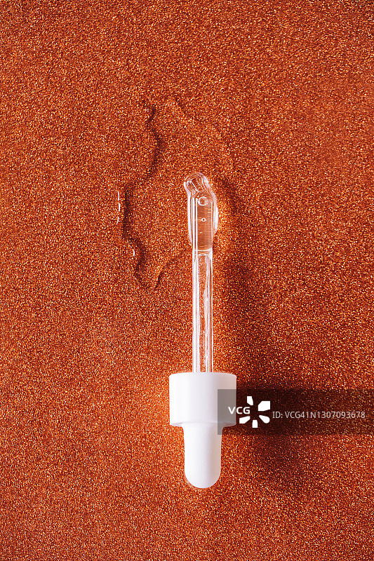 滴管附近的精华液或透明质酸滴在闪光古铜色背景上，年度潮流程序，健康与保健理念图片素材