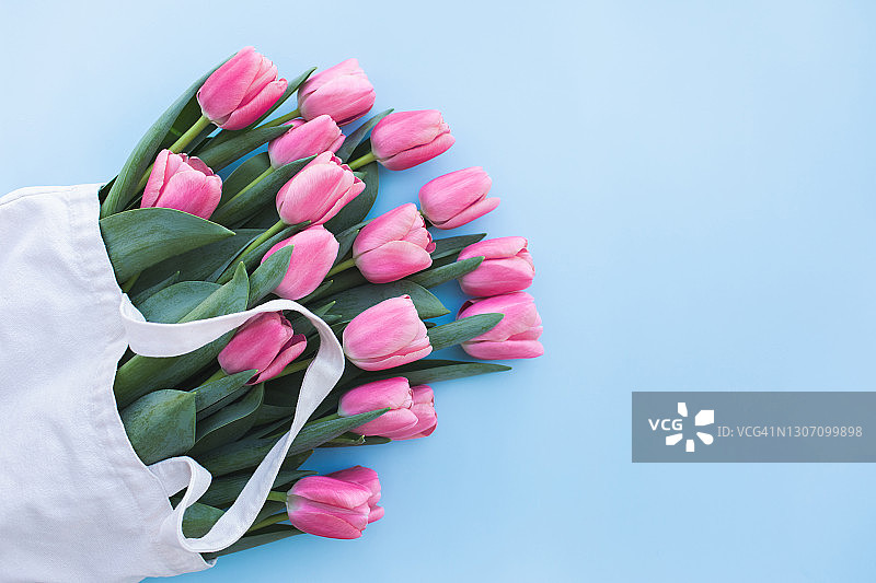 浅蓝色背景上的环保购物袋里的粉色郁金香图片素材