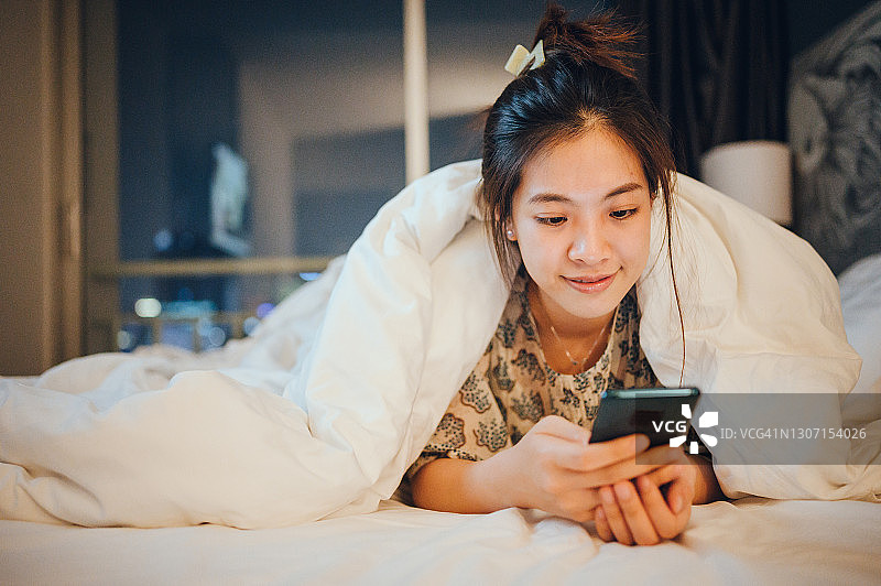 在家躺在床上使用智能手机平板电脑的年轻亚洲女性，放松和度假图片素材