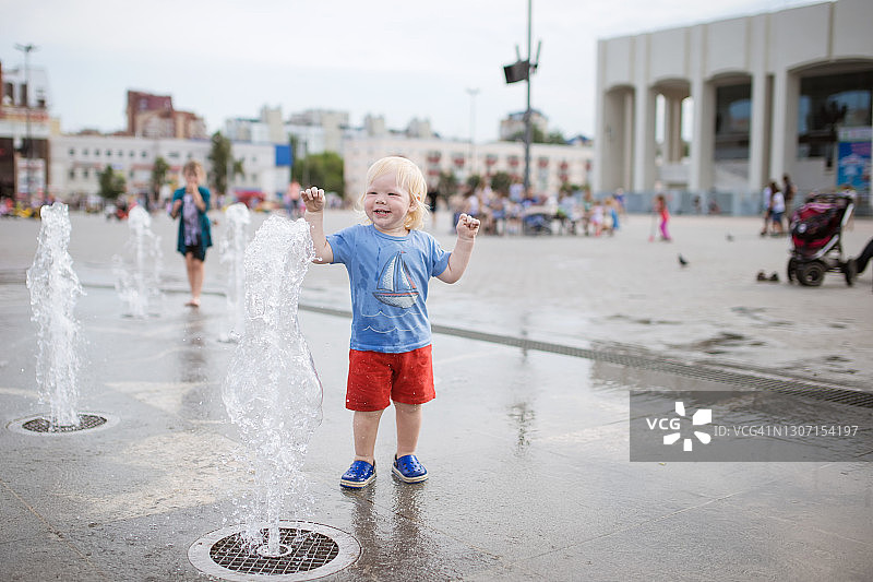小男孩在街上喷泉附近玩水图片素材