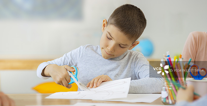 男孩用剪刀剪图画纸图片素材