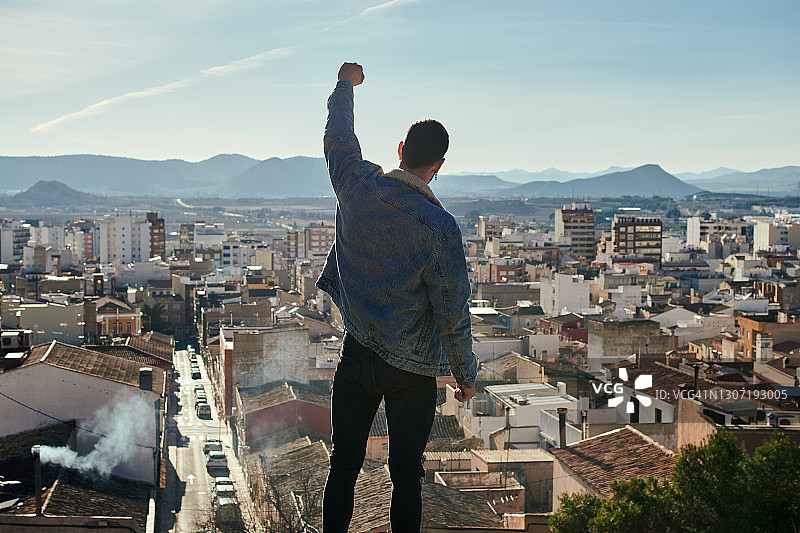 男人在屋顶上俯瞰城市，举起拳头图片素材