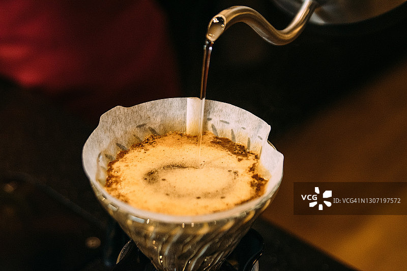 在咖啡馆里，将水倒入咖啡滤纸中图片素材