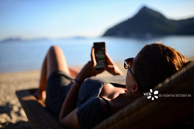 年轻女人在沙滩上使用智能手机图片素材