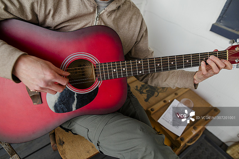 男子弹奏红色木吉他特写，旁边放着空酒杯图片素材