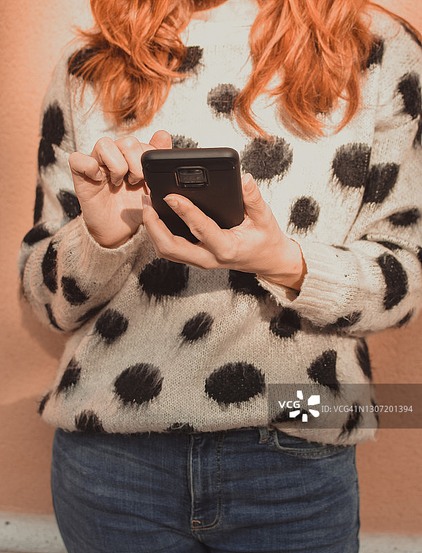 女人手持手机，背景为黑色圆点针织衫和红色头发图片素材